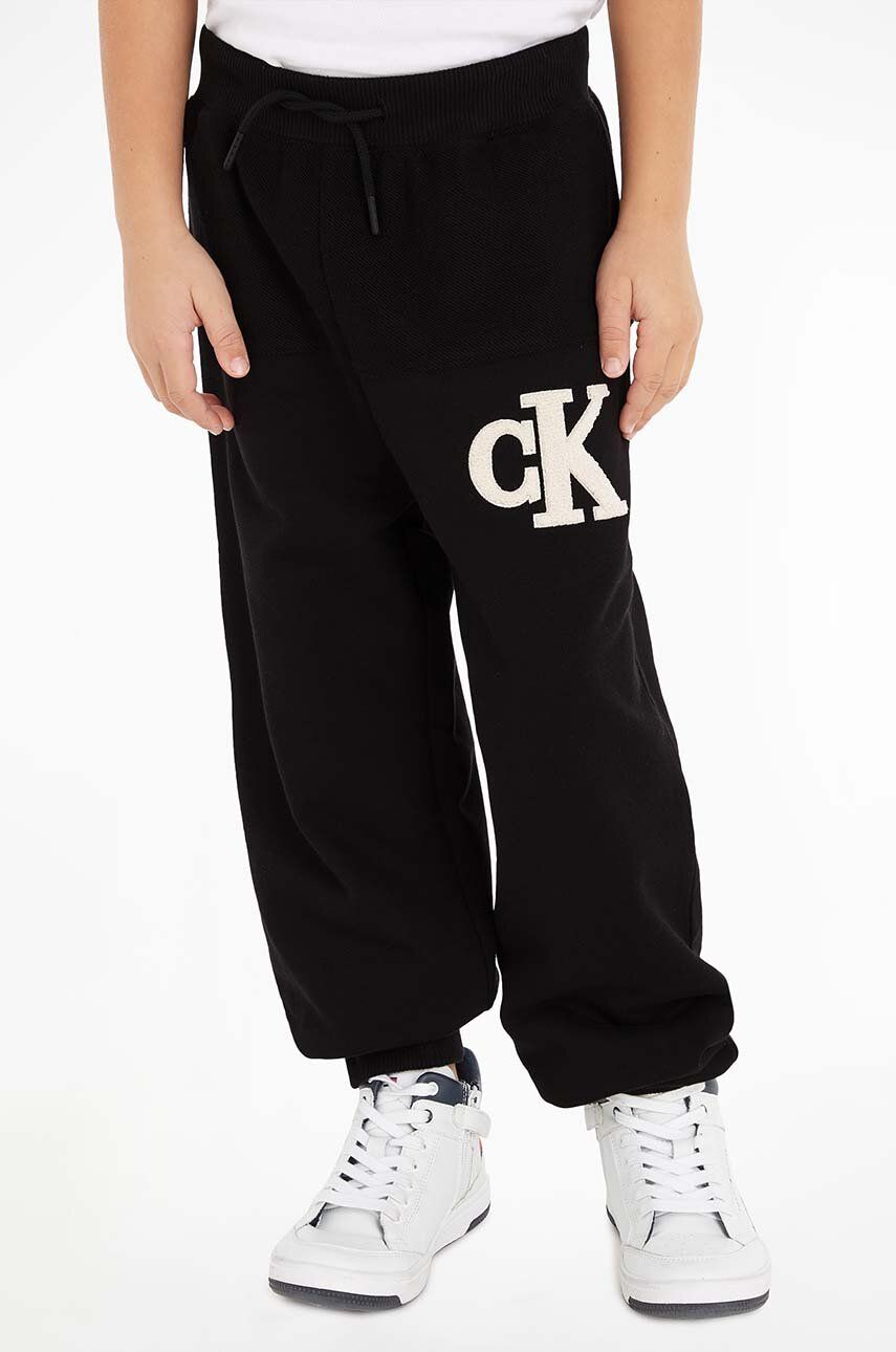 Levně Dětské bavlněné tepláky Calvin Klein Jeans černá barva, s aplikací