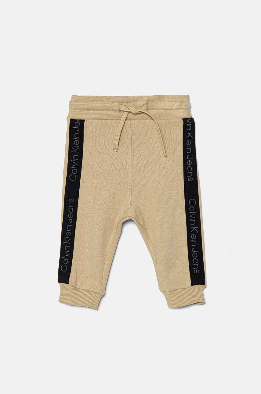 Levně Kojenecké bavlněné tepláky Calvin Klein Jeans béžová barva, s aplikací, IN0IN00194