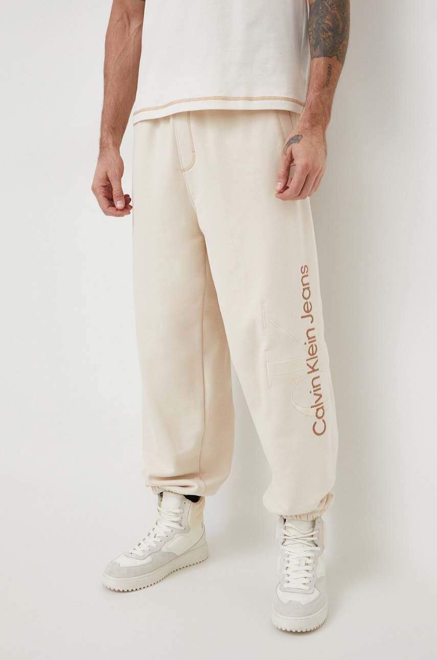 Levně Bavlněné tepláky Calvin Klein Jeans béžová barva, s aplikací, J30J324953